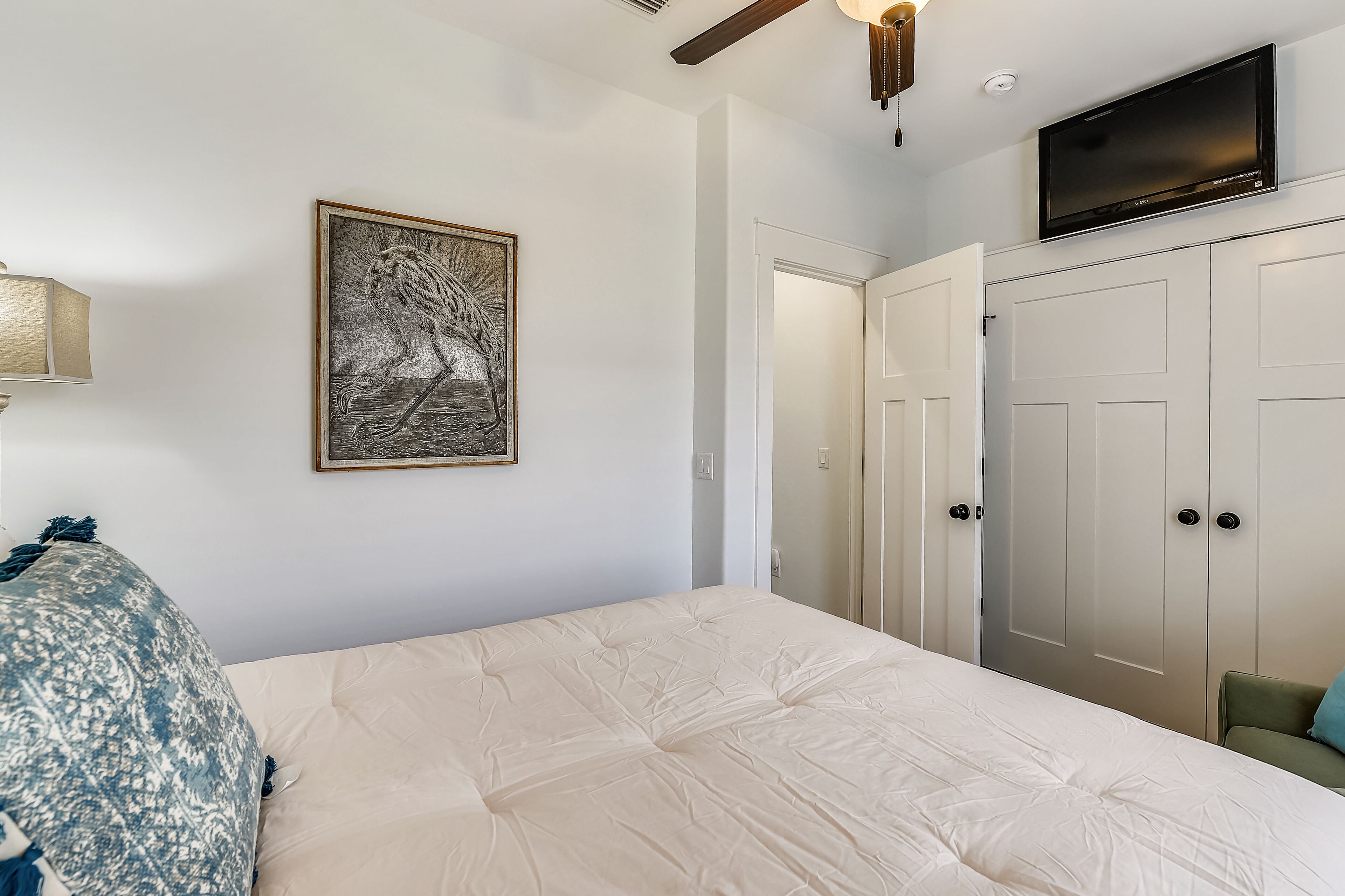 A bedroom with a bed, a television mounted above a wardrobe, and a framed artwork on the wall.
