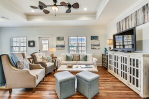 A spacious living room with a high ceiling, a large TV, and a white cabinet. - Sandy Feet Retreat by Book That Condo (Panama City Beach)
