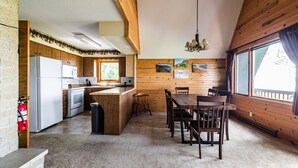 A cozy cabin-style kitchen with wooden walls, a central island, and a dining area. -  Riverview Cabin home! (Stoddard)