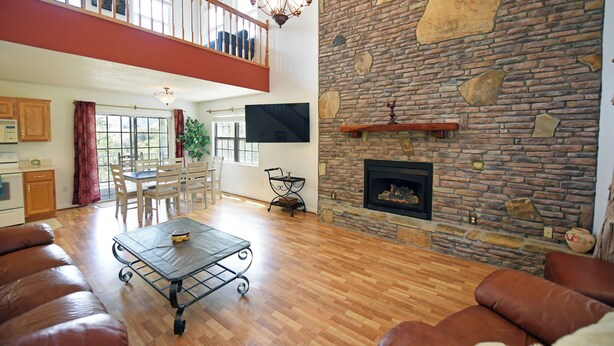 A spacious living area with a stone fireplace, wooden flooring, a dining area, and a high ceiling with a staircase. - Spacious Family Mountain Gem Nestled in Nature-5 min to Historic Murphy!  (Murphy)