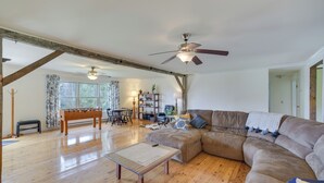 Ein geräumiges Wohnzimmer mit Holzboden, einem großen Ecksofa, einem Couchtisch und einem Deckenventilator.