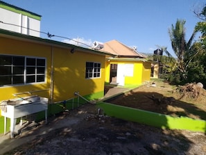 A yellow building with a green roof, a visible window, and a small outdoor area with a bench.