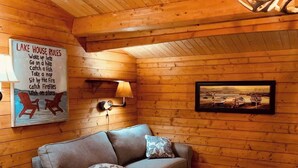 Una habitación acogedora tipo cabaña con techo de madera, un sofá, una mesita y una cama. Un letrero con la inscripción 'Lake House Rules' es visible en la pared.