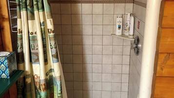 A shower area with a curtain featuring currency notes, tiled walls, and a shelf with toiletries.