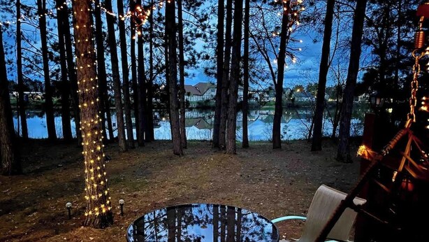 Una terraza al aire libre con una mesa redonda y sillas, rodeada de árboles y vista a un lago.