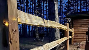 Una cerca de madera con luces de cadena en un área boscosa.