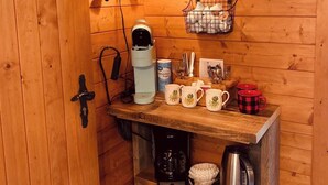 Interior de una cabaña de madera con una estación de café, tazas y un cartel que dice '¡ZOCO TU SALTO AL RÍO!'.
