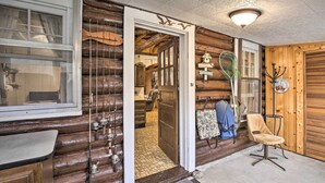 A log cabin interior with a wooden exterior, a fishing rod display, a chair, and a small table. - Lakefront 1930’s Log Cabin w/ Dock & Fire Pit! (Rice Lake)