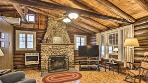 A log cabin interior with a stone fireplace, wooden walls, a ceiling fan, and a television. - Lakefront 1930’s Log Cabin w/ Dock & Fire Pit! (Rice Lake)