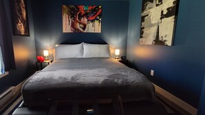 Ein Schlafzimmer mit einem Bett, zwei Nachttischen mit Lampen, einem Fenster mit Jalousien und Bildern an den Wänden.