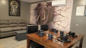 Ein Essbereich mit einem Holztisch, gedeckt für vier Personen, einem grauen Sofa und einem großen Wandbild mit einem Elefanten.