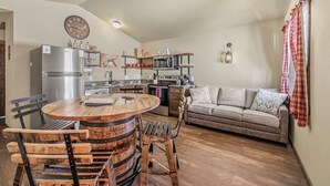 A compact kitchen with a central island, a refrigerator, microwave, and a dining area with wooden chairs. - Family-Friendly Old West Cabin Near YNP (Island Park)