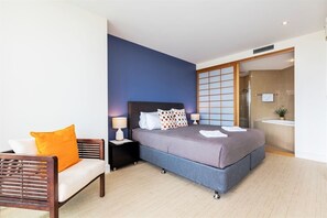 Ein modernes Hotelzimmer mit einem großen Bett, einer Couch und einer Glastür zum Badezimmer.