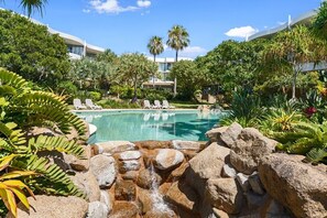 Ein Poolbereich mit Liegestühlen, einer Wasserfallanlage und üppiger Bepflanzung.