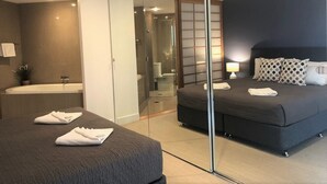 A modern hotel room with a large bed, a separate bathroom with a bathtub, and a sliding glass door leading to a walk-in closet.