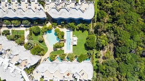 An aerial view of a resort with multiple buildings, a central swimming pool, and surrounding greenery.