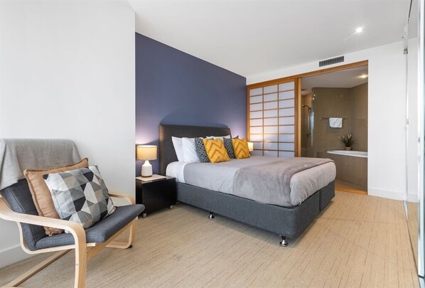Ein modernes Hotelzimmer mit Bett, Nachttisch, Stuhl und Blick ins Bad.