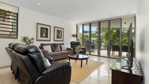 A modern living room with a leather sofa, a brown couch, and a coffee table. There are framed pictures on the wall and a large sliding glass door leading to an outdoor area.