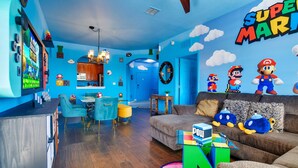 Un salón vibrante con decoración temática de Nintendo, incluyendo un mural de Super Mario, peluches y una consola de juegos.