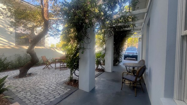 A covered outdoor seating area with a table and chairs, a tree, and a car parked in the background. - Mediterannean Home Steps to 30As Longest Public Beach,Private Pool,Courtyard (Santa Rosa Beach)