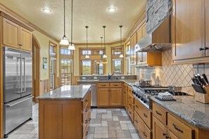Une cuisine spacieuse dotée de plans de travail en granit, d’appareils électroménagers en acier inoxydable, d’armoires en bois et de luminaires suspendus.