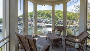 Un espace extérieur abrité, aménagé avec des meubles en osier, un ventilateur de plafond et offrant une vue sur une rivière et des maisons.