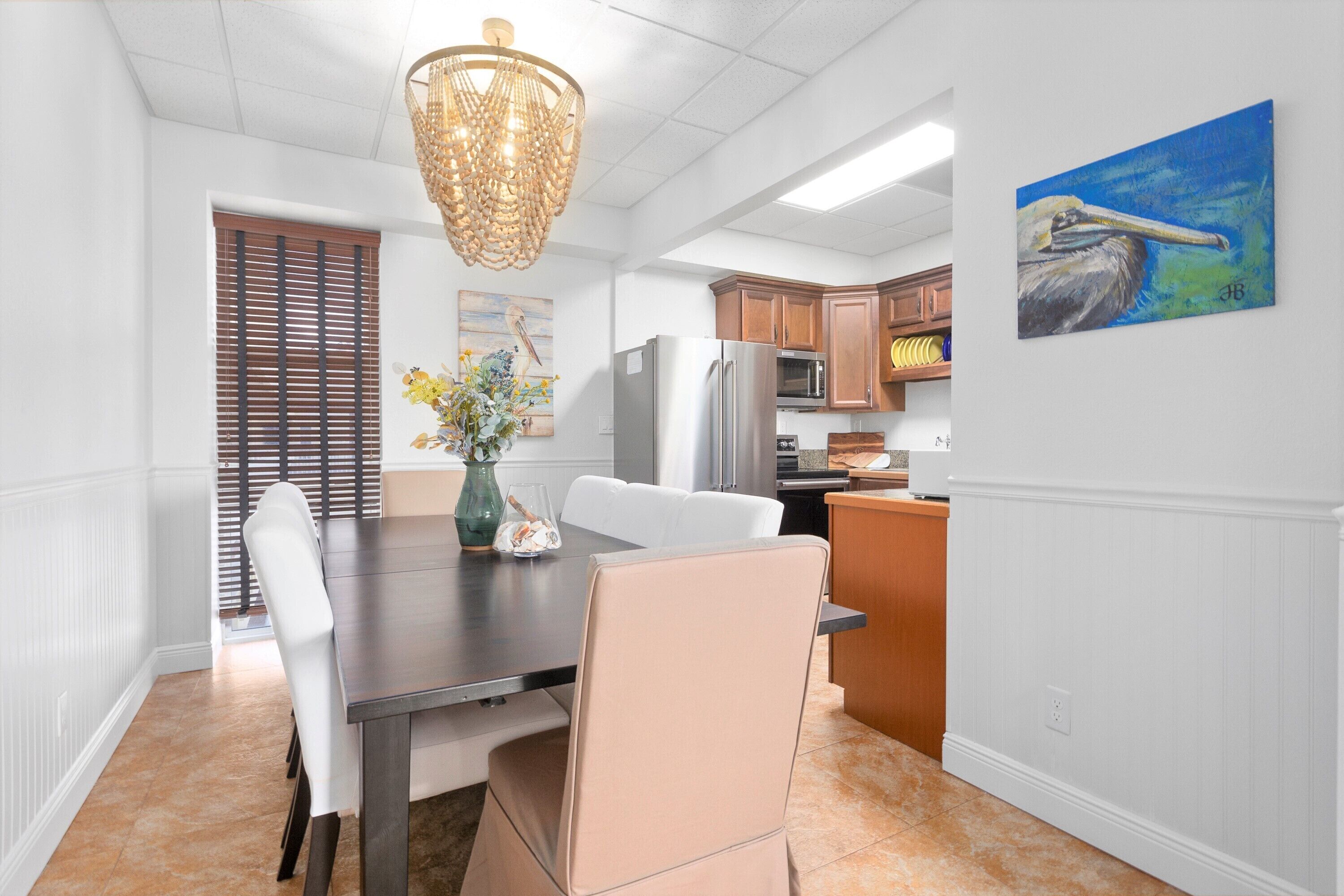 Una cocina moderna con armarios blancos, un refrigerador de acero inoxidable y un comedor con mesa de madera oscura y sillas blancas.
