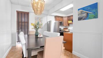 Una cocina moderna con armarios blancos, un refrigerador de acero inoxidable y un comedor con mesa de madera oscura y sillas blancas.