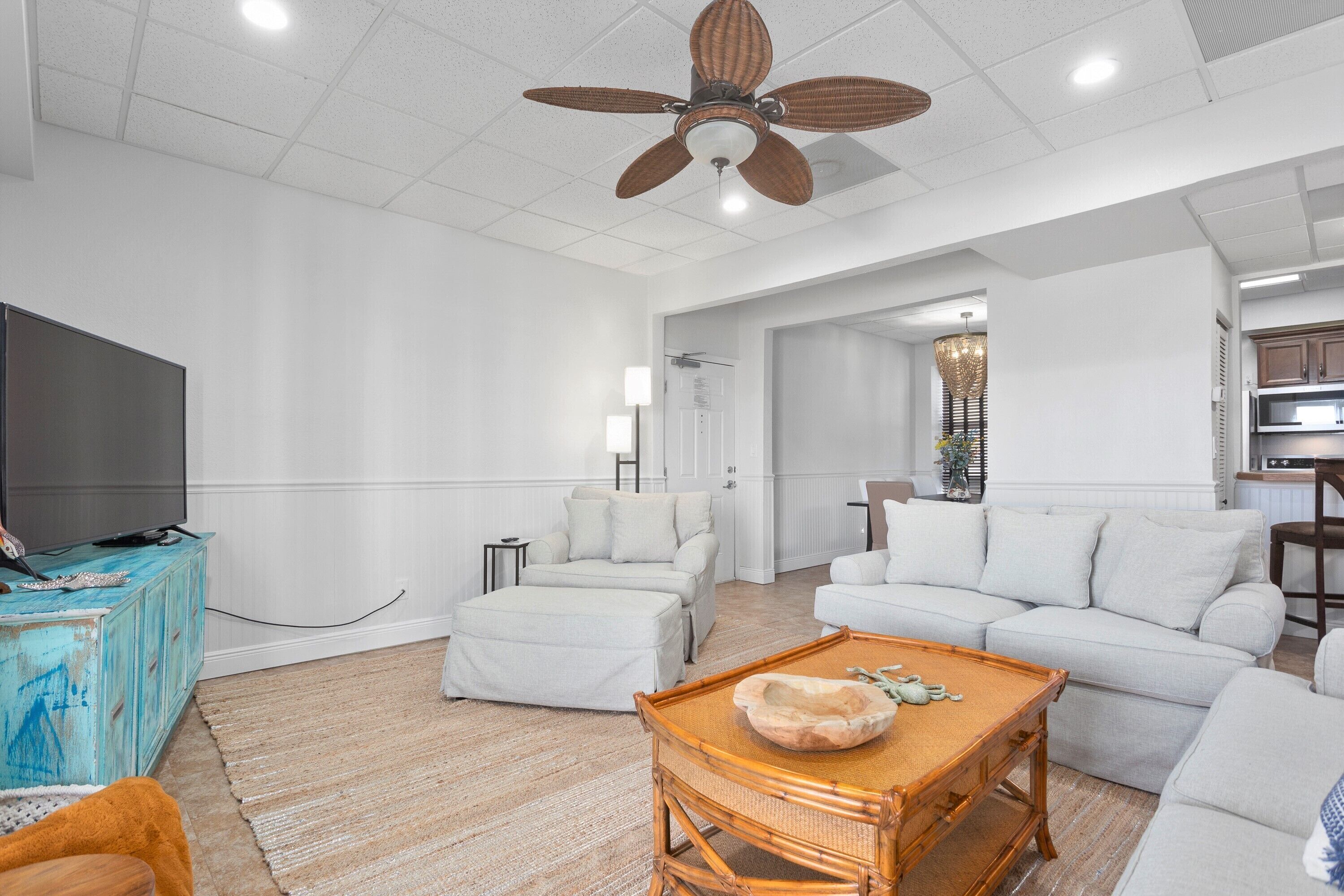 A spacious living room with a large flat-screen TV, a ceiling fan, and a billiards table.