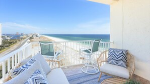 Un balcon avec vue sur la plage et l’océan, aménagé avec des fauteuils et des coussins en osier.