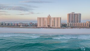 Un hôtel en bord de mer, avec plusieurs étages, une plage au premier plan et un ciel dégagé.