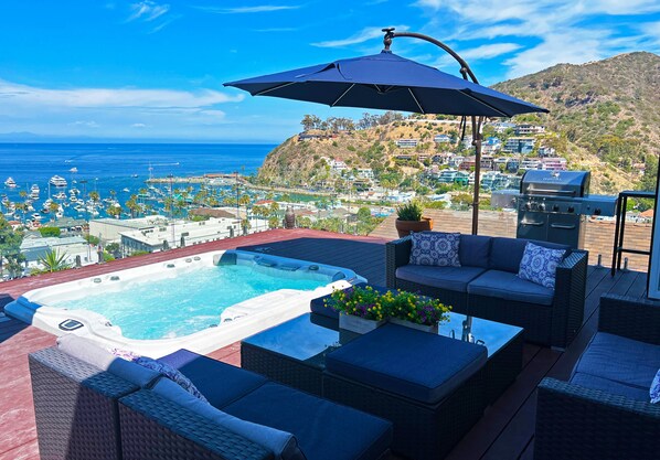Terraza en la azotea con jacuzzi, mobiliario exterior y vistas al océano y al pueblo en la colina.