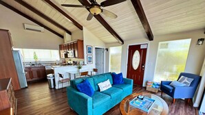 A spacious living room with a teal sofa, a coffee table, and a dining area with a kitchen in the background.
