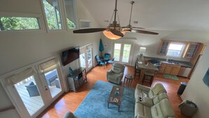 Uma sala de estar ampla com pé direito alto, área de jantar e cozinha. Escada leva a um andar superior.