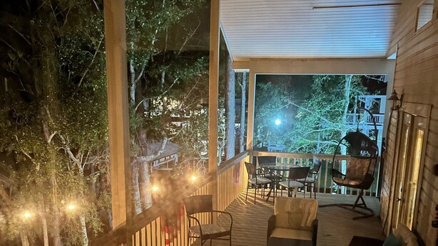 Um deck de madeira com mobiliário externo, vista para as árvores ao redor e uma varanda com corrimão.