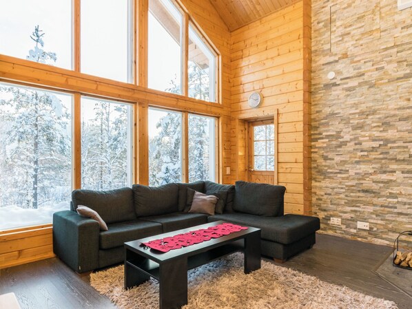 A cozy cabin interior with a large window, a stone wall, and a dark-colored sofa.