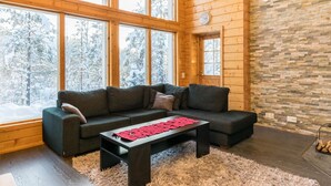 Una sala de estar acogedora con un sofá modular, una mesa de centro y ventanas amplias que ofrecen vistas a árboles cubiertos de nieve.