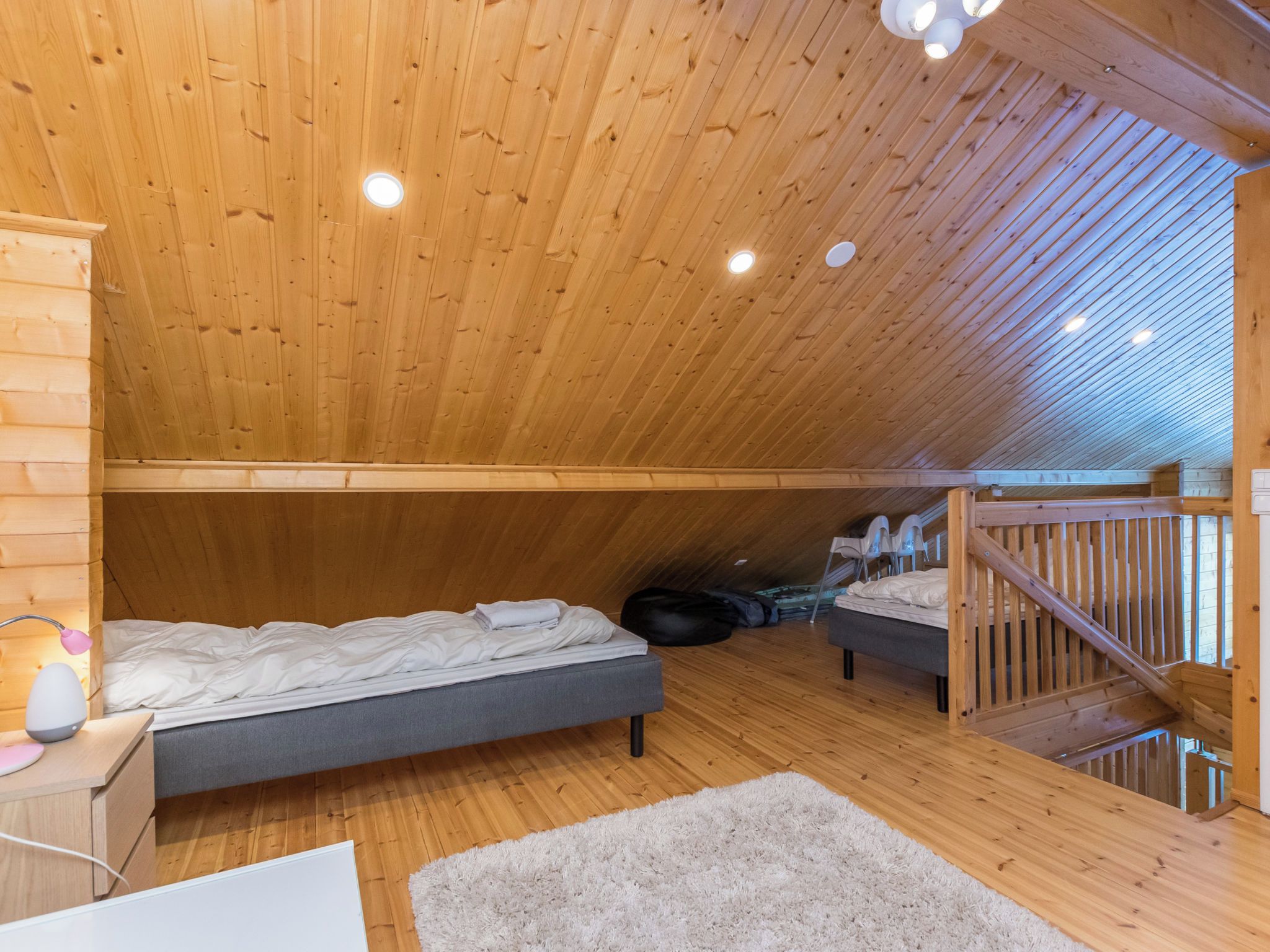 A loft bedroom with a sloped ceiling, wooden walls, two beds, a desk, and a staircase.