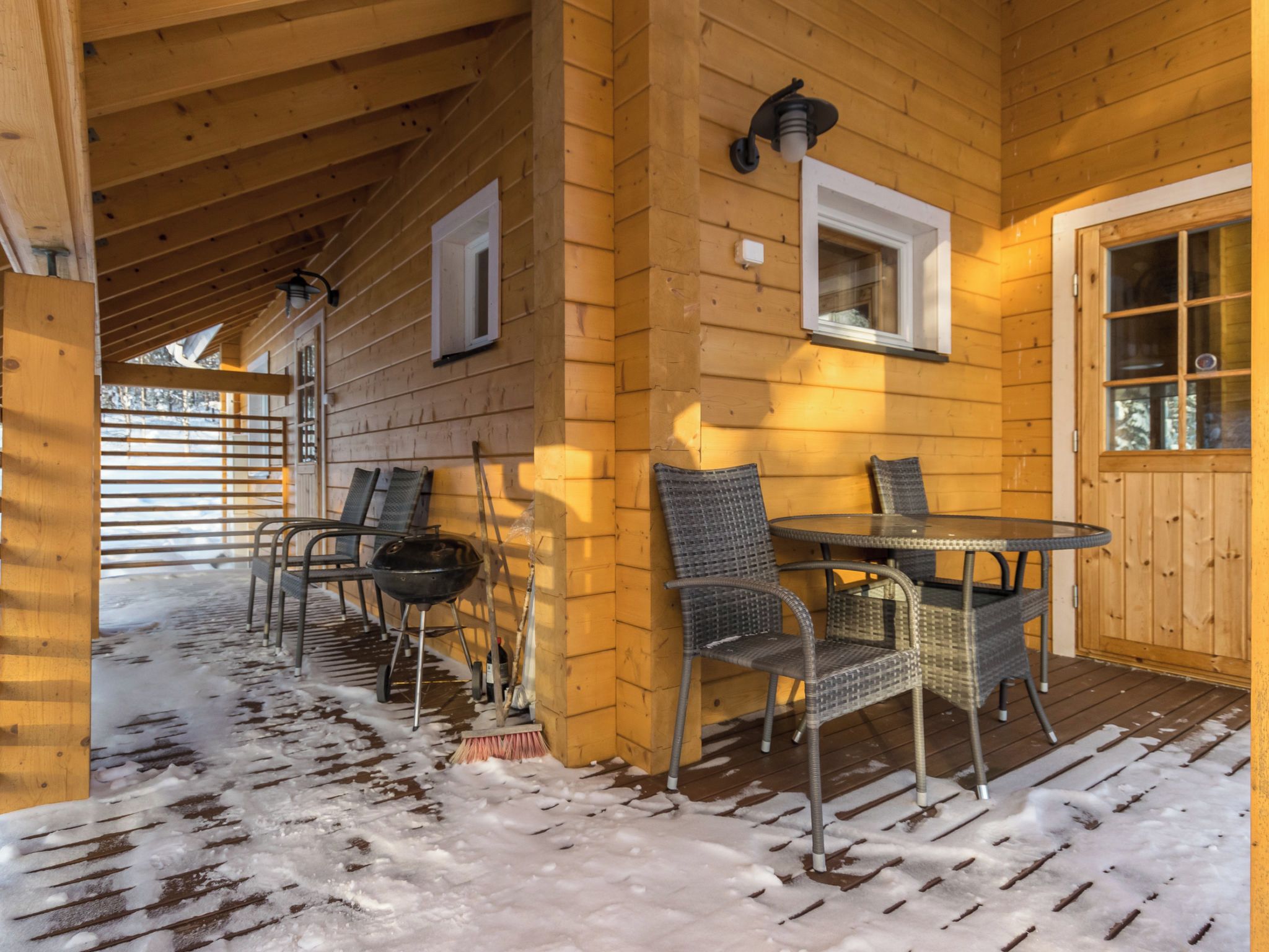 A wooden cabin with a covered porch, outdoor seating, and a snow-covered floor.