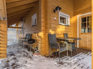 Une cabane en bois dotée d’un porche couvert, de sièges d’extérieur et d’un plancher recouvert de neige.