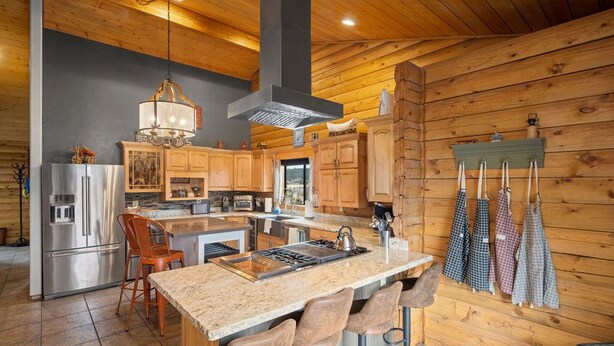 A kitchen with wooden walls, a central island with bar stools, stainless steel appliances, and hanging kitchen towels. - Summer Retreat, Dog Friendly, Fenced Yard, Hot Tub, Game Room, Fire Pit (Flagstaff)