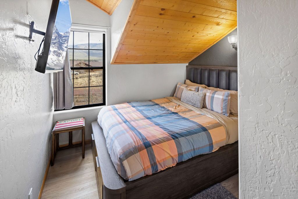Ein Schlafzimmer mit Bett, Fenster, einem kleinen Tisch und einer Holzbalkendecke.