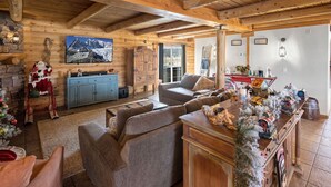 A cozy log cabin interior with a fireplace, a sofa, a wooden dining table, and a Christmas tree. - Summer Retreat, Dog Friendly, Fenced Yard, Hot Tub, Game Room, Fire Pit (Flagstaff)