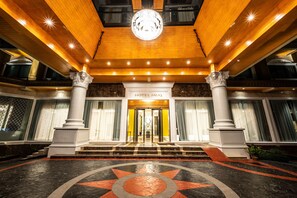 A grand hotel entrance with a star-patterned floor, a chandelier, and a sign reading "HOTEL MUQ".
