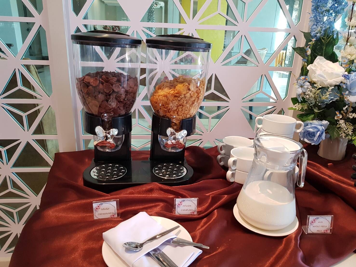 A breakfast buffet with two dispensers of cereal and a pitcher of milk.