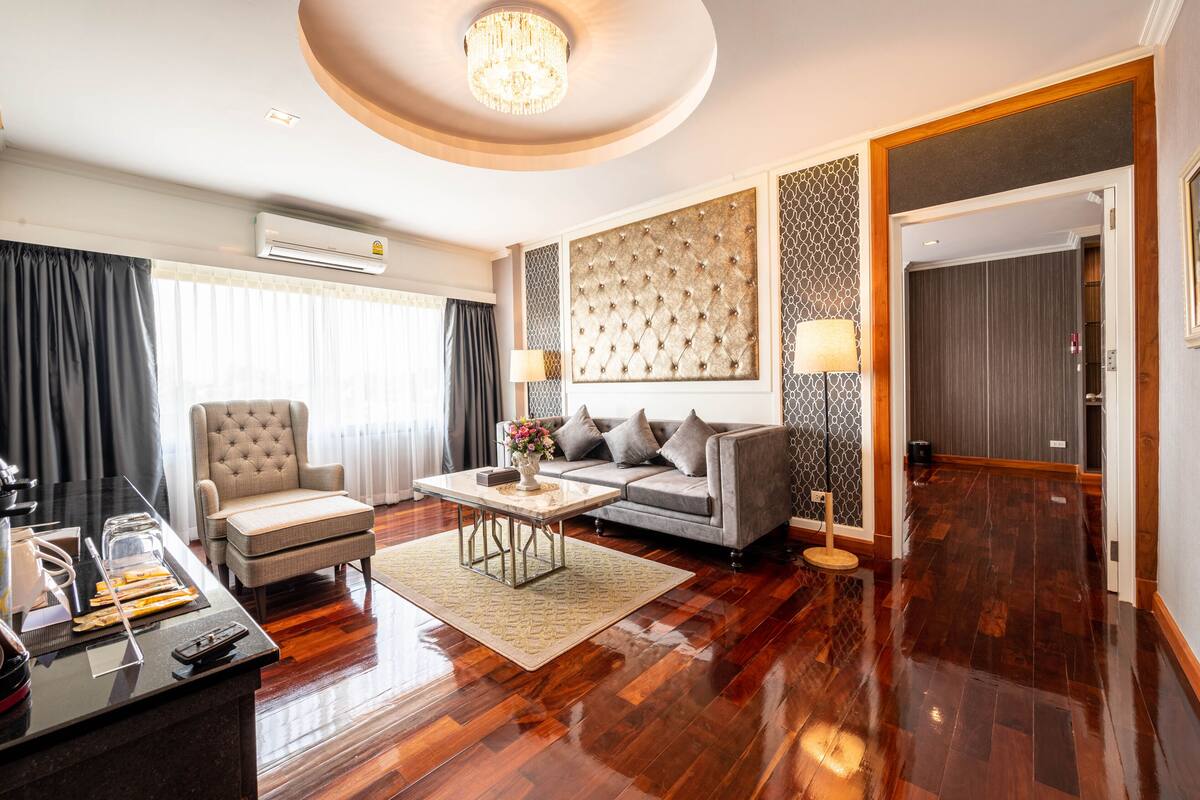 A modern hotel room with a plush sofa, a coffee table, a side table, and a large window with curtains.