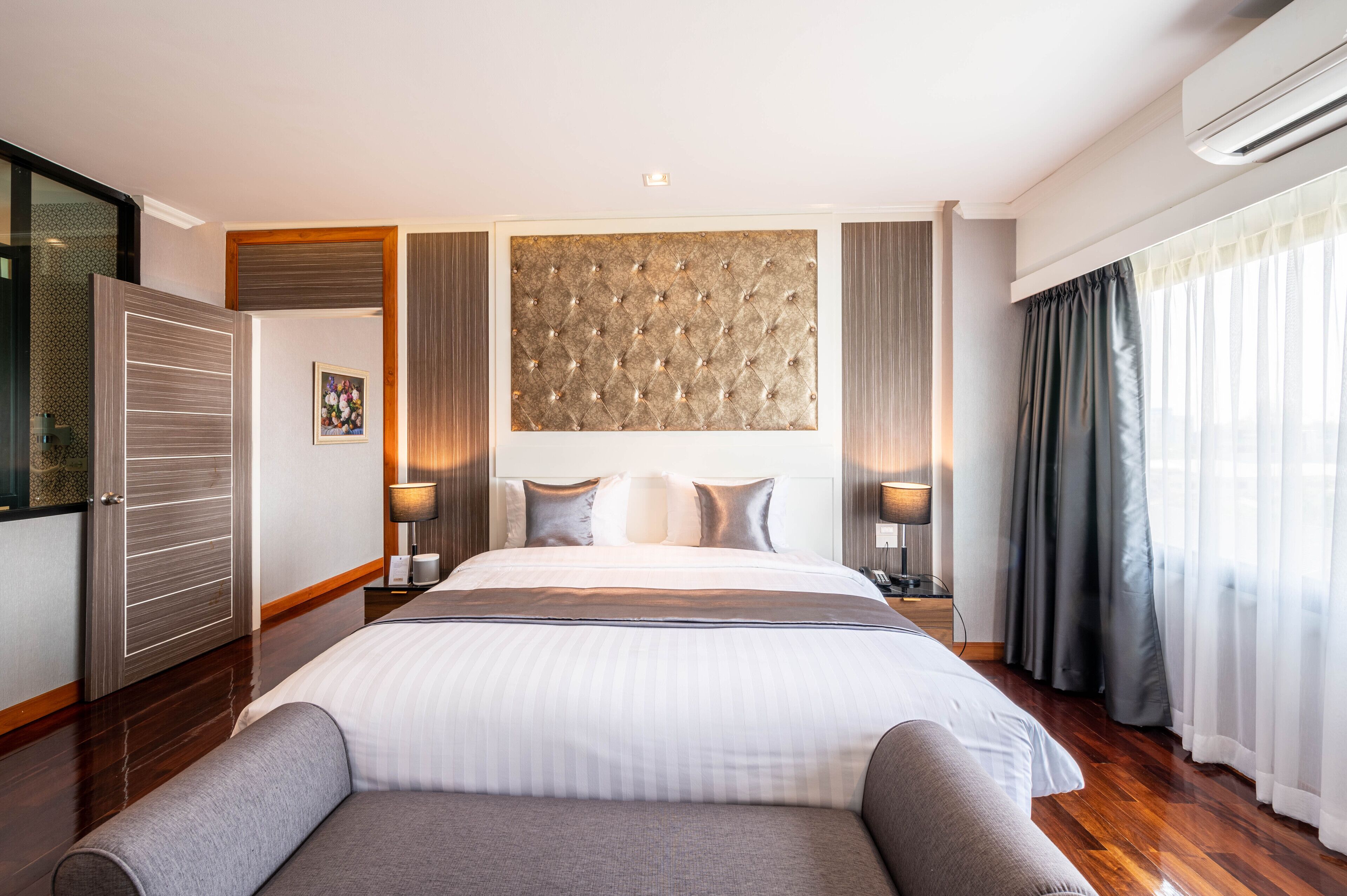 Hotelkamer met groot bed, een hoofdbord met een gestuikt ontwerp, nachtkastje met lamp, een kledingkast en een raam met gordijnen.