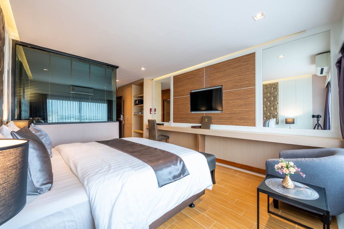A modern hotel room with a large bed, a desk, a flat-screen TV, and a seating area.