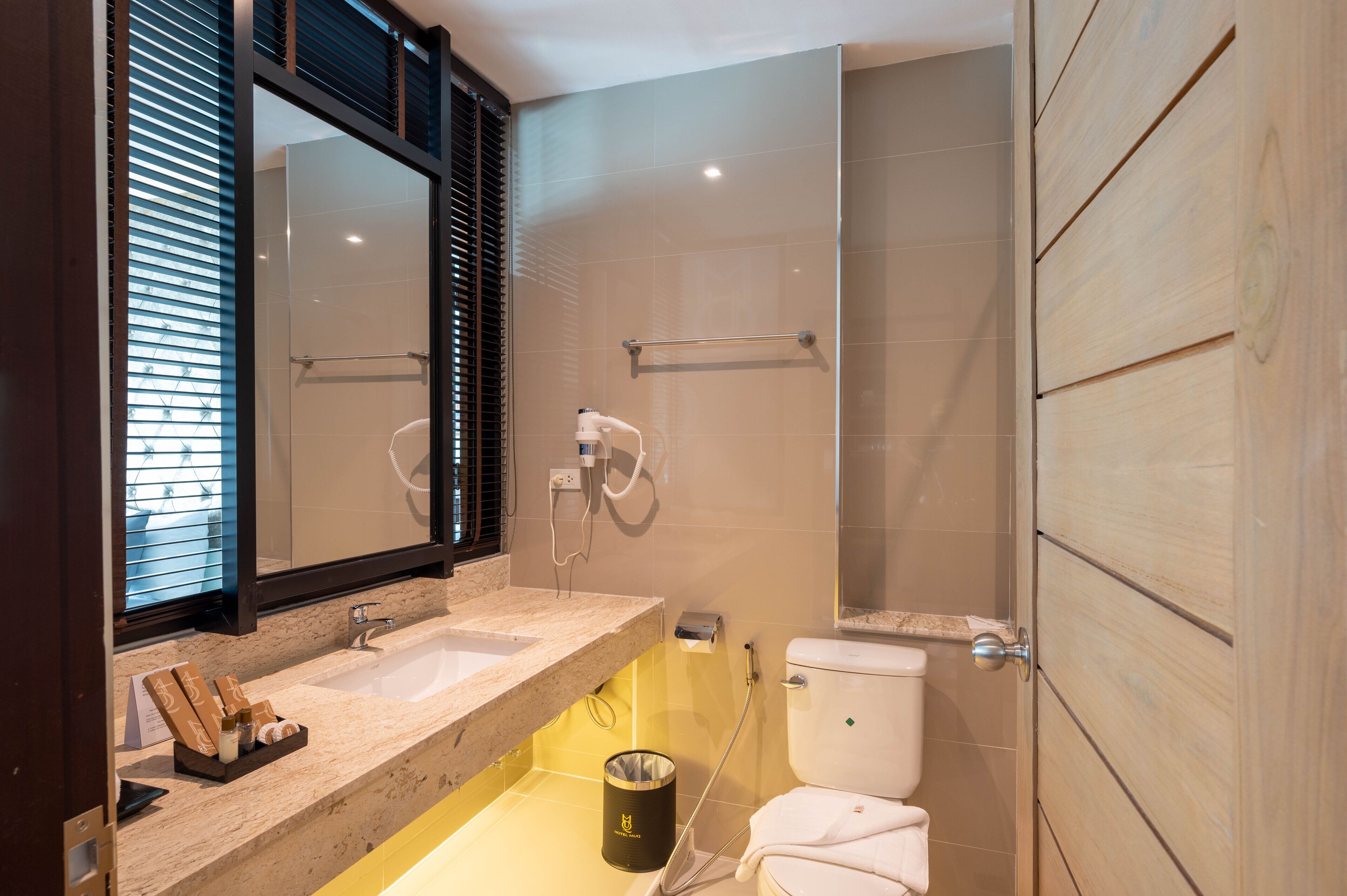 A modern bathroom with a large mirror, a sink with toiletries, a shower, and a toilet.