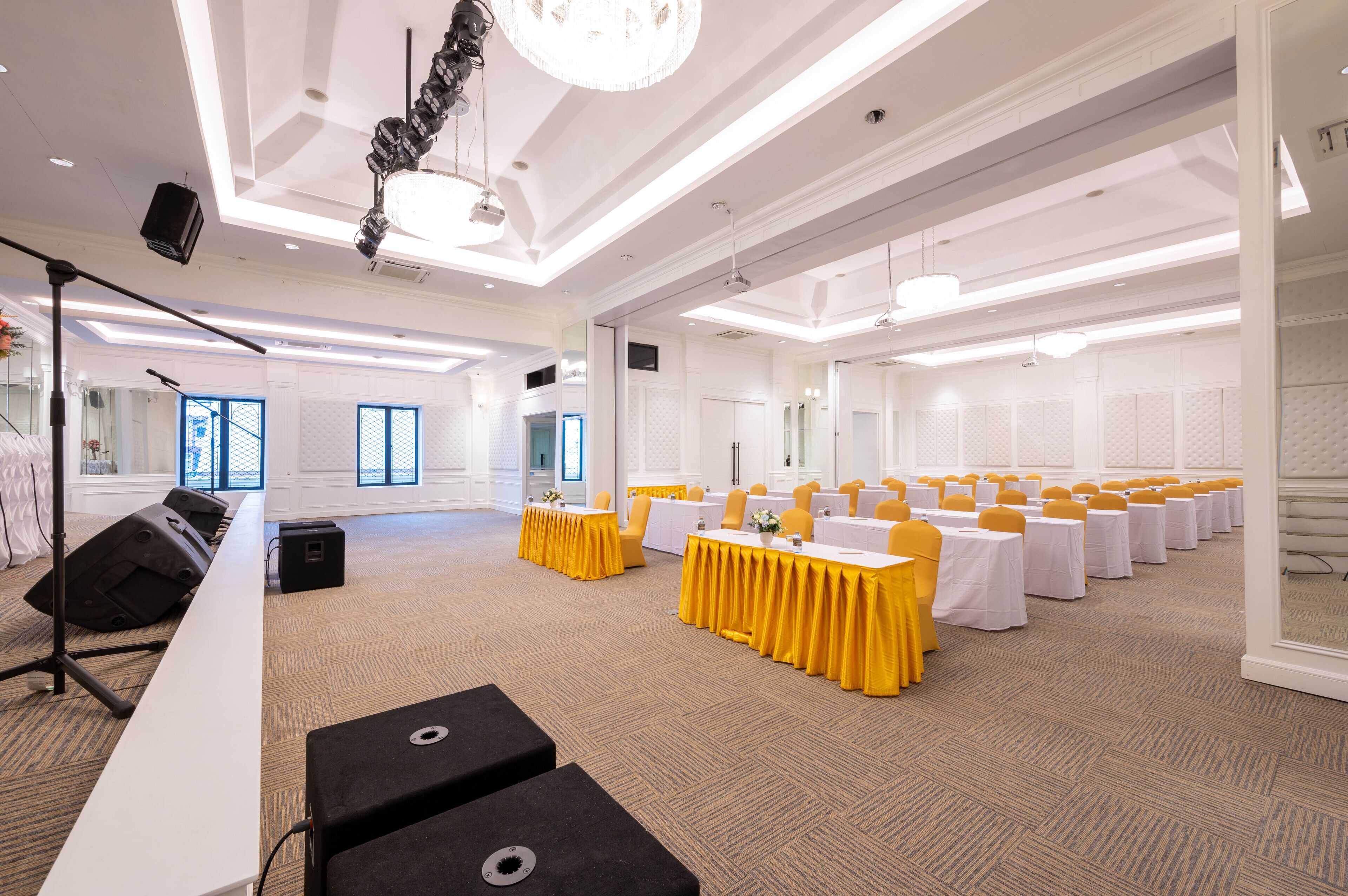 A conference room with rows of tables, yellow chairs, and a stage with a microphone.
